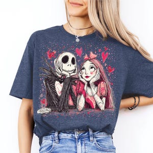 A woman wearing a blue t-shirt with a graphic design featuring a skeleton and a woman with a heart-shaped headband.