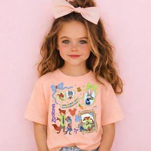 A young girl with long brown hair wearing a pink bow and a pink t-shirt with various cartoon characters and designs.
