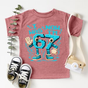 A pink t-shirt with a graphic design featuring a character made up of numbers, along with a pair of sneakers and a camera.