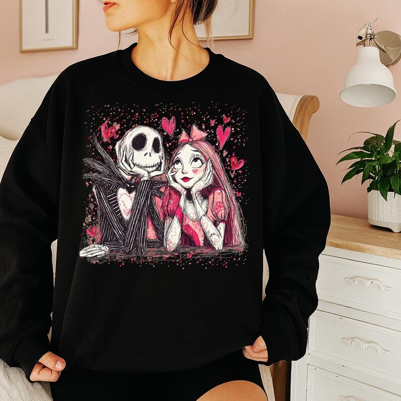 A woman wearing a black sweatshirt with a graphic design featuring a skeleton and a woman with a pink bow.