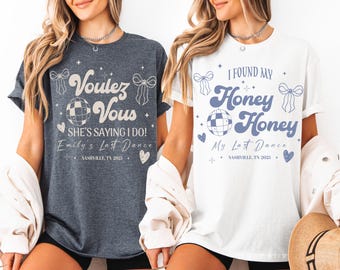 May include: Two t-shirts, one dark gray and one white, with matching text and graphics. The dark gray shirt says "Voulez Vous" and "She's Saying I Do!" The white shirt says "I Found My Honey Honey." Both shirts have a disco ball graphic.