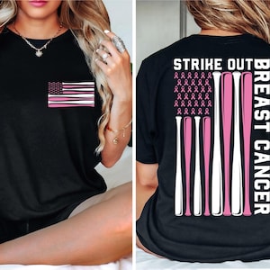 May include: Black t-shirt with a pink ribbon design and the text "Strike Out Breast Cancer". The front of the shirt features a pink ribbon American flag design.