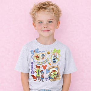 A young boy with blonde hair is smiling and wearing a gray t-shirt with a colorful graphic design featuring various cartoon characters and elements.