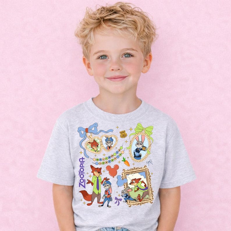 A young boy with blonde hair is smiling and wearing a gray t-shirt with a colorful graphic design featuring various cartoon characters and elements.