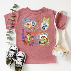 a pink t-shirt with a cartoon character design, a pair of black and white sneakers, and a small wooden camera.