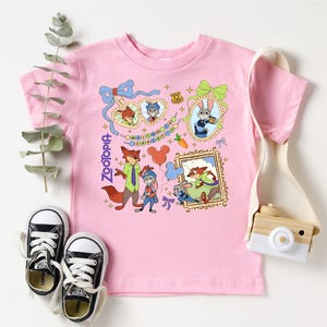 a pink t-shirt with a cartoon character design, a pair of black and white sneakers, a white camera, and some greenery.