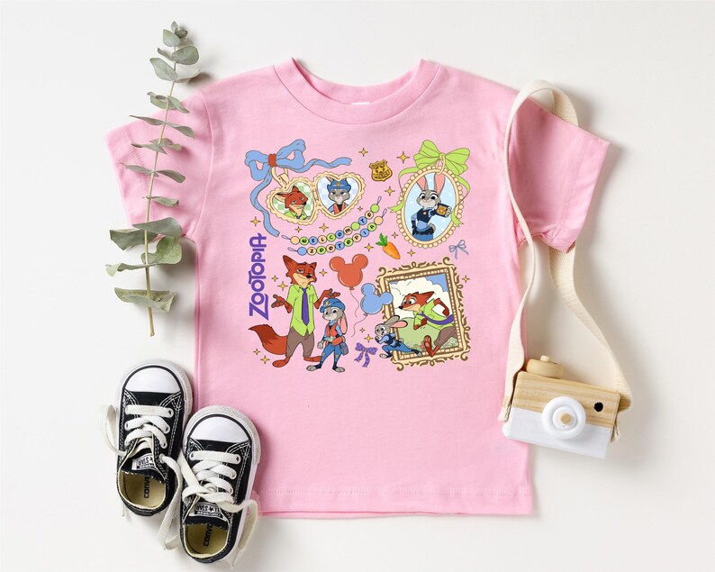 a pink t-shirt with a cartoon character design, a pair of black and white sneakers, a white camera, and some greenery.