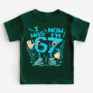 A green t-shirt with a graphic design featuring a robot character and text that says "I WAS NOW IM".
