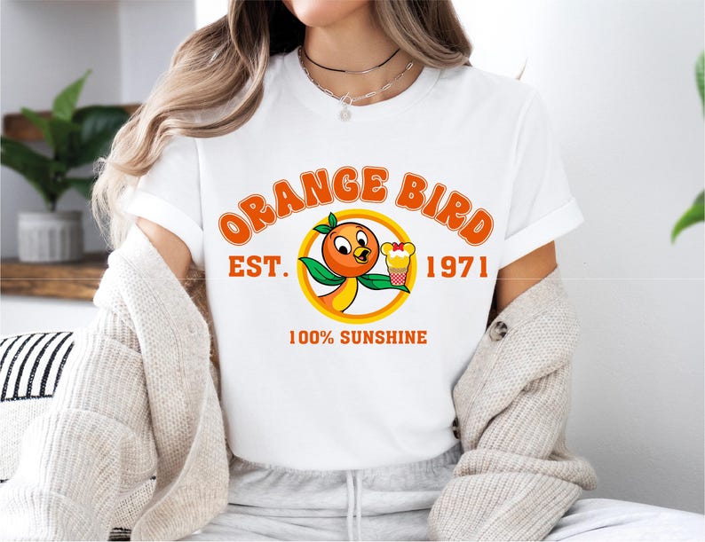 a woman sitting on a bed wearing an orange bird t - shirt