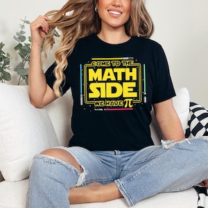 Op de afbeelding: Een zwart T-shirt met een gele afbeelding waarop staat "Come to the Math Side We Have Pi" met lichtblauwe, groene en roze lichtzwaarden.