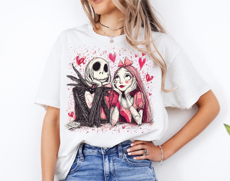 A woman wearing a white t-shirt with a graphic design featuring a skeleton and a woman with a heart-shaped bow on her head.