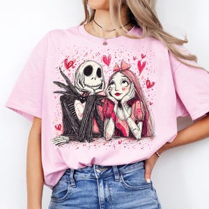 A woman wearing a pink t-shirt with a graphic design of a skeleton and a girl with a heart-shaped headband.