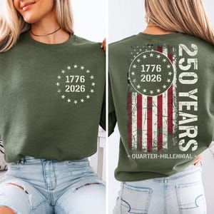 A woman wearing a green sweatshirt with a graphic design on the back. The design features a circle with the numbers 1776 and 2026, and an American flag pattern.