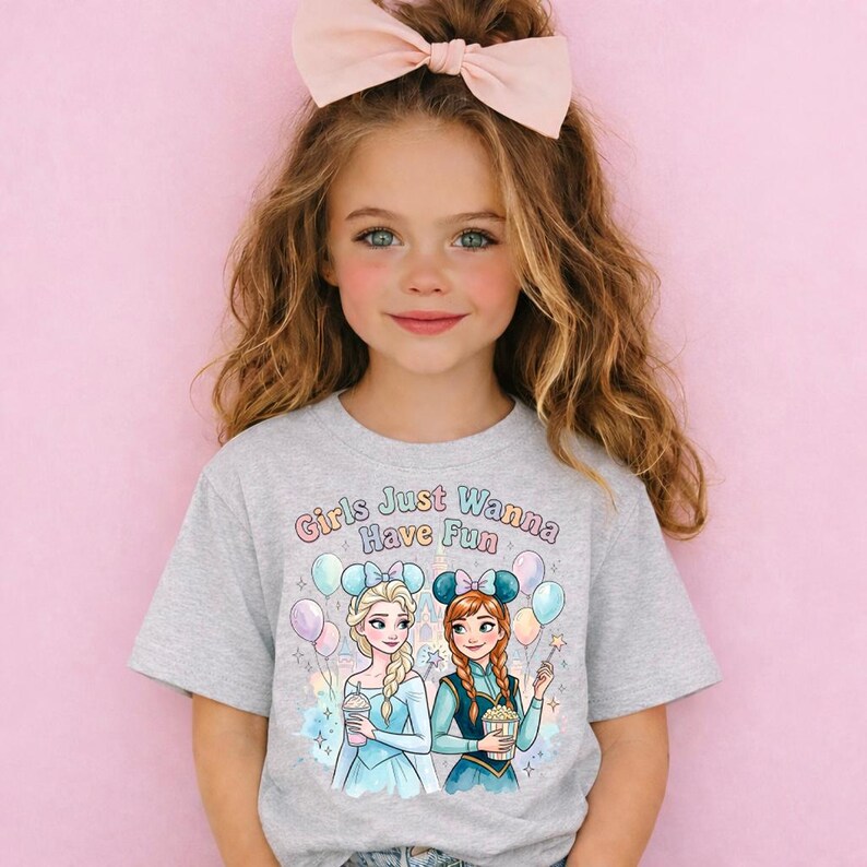 A young girl with long brown hair wearing a gray t-shirt with a graphic of two cartoon girls and the text "Girls Just Wanna Have Fun" printed on it.