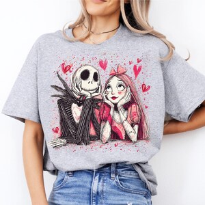 A woman wearing a grey t-shirt with a graphic design featuring a skeleton and a woman with a pink bow.