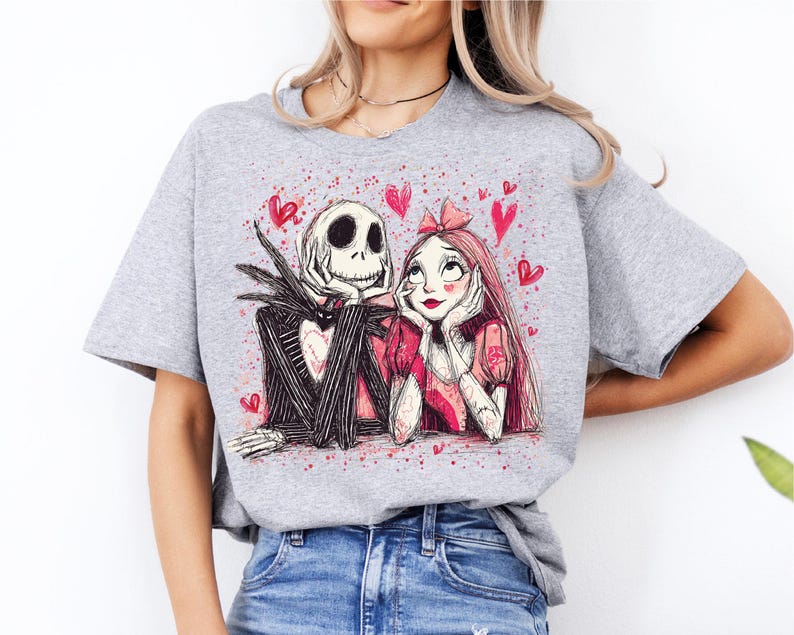 A woman wearing a grey t-shirt with a graphic design featuring a skeleton and a woman with a pink bow.