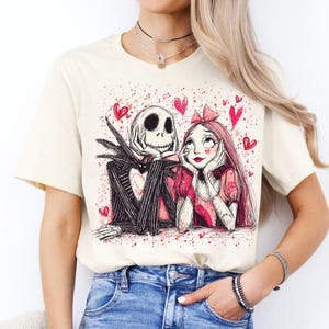 A woman wearing a white t-shirt with a graphic design featuring a skeleton and a woman with a pink bow.