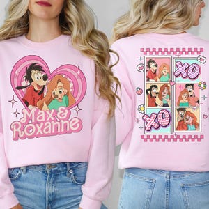 May include: Pink sweatshirt with a heart-shaped graphic featuring Max and Roxanne from the Disney movie A Goofy Movie. The graphic includes the text "Max & Roxanne". The back of the sweatshirt features a grid of four cartoon images of Max and Roxanne with the text "XO" in each image.