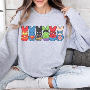 May include: A gray sweatshirt with a graphic of six Peeps shaped like superheroes. The Peeps are wearing costumes of Iron Man, Superman, Batman, Hulk, Spiderman, and Captain America.
