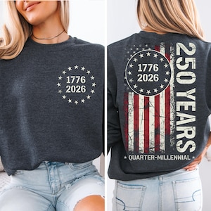 a woman wearing a grey sweatshirt with a graphic design on the back. The design includes a circle with the numbers 1776 and 2026, and an American flag pattern.