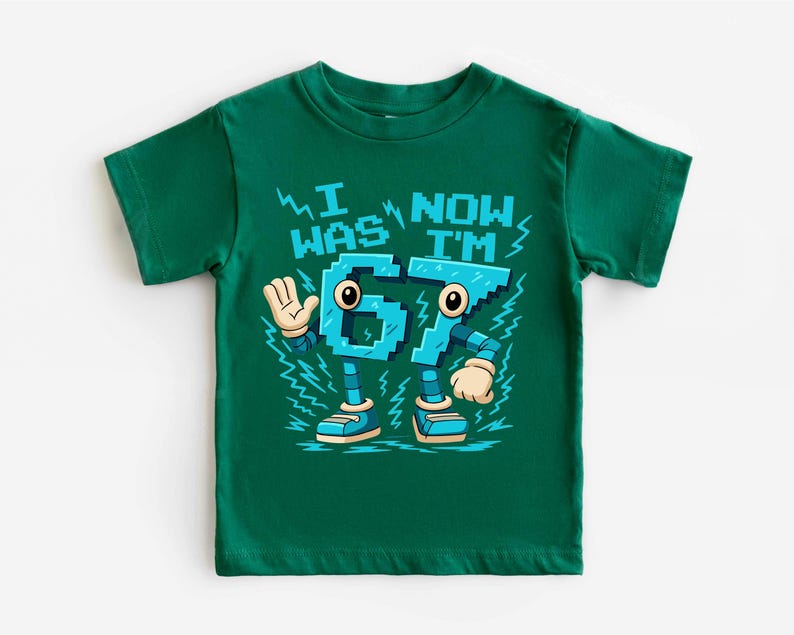 A green t-shirt with a graphic design featuring a robot character and text that says "I WAS NOW I'M 67".