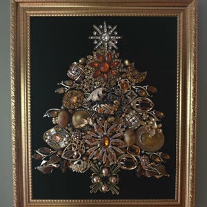 Könnte beinhalten: Ein gerahmtes Wandbild in Form eines Weihnachtsbaums, zusammengesetzt aus einer Auswahl an vintage Schmuckstücken in Bernstein-, Gold- und Bronzetönen, darunter Broschen und Strasssteine, auf schwarzem Grund in einem Goldrahmen.