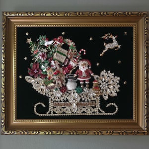 Könnte beinhalten: Ein gerahmtes Wandbild mit einer Weihnachtsschlitten-Collage aus Vintage-Schmuck. Das Design umfasst eine Weihnachtsmannfigur, einen Schneemann, ein Rentier und einen Baum, verziert mit klaren und farbigen Strasssteinen auf schwarzem Samt.
