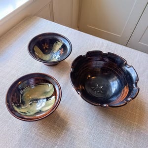 May include: Three ceramic bowls with brown and black glaze. The bowls have a unique design with a star-shaped pattern and a light green and yellow glaze.