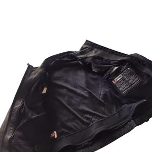 Może przedstawiać: Czarna sk&oacute;rzana kurtka motocyklowa z zapięciem na zamek błyskawiczny i wieloma wewnętrznymi kieszeniami. Wnętrze kurtki jest wyłożone czarną siateczką. Wewnątrz kurtki widoczna jest metka z tekstem.