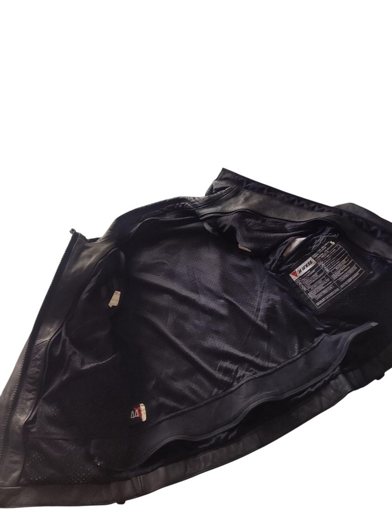 Może przedstawiać: Czarna sk&oacute;rzana kurtka motocyklowa z zapięciem na zamek błyskawiczny i wieloma wewnętrznymi kieszeniami. Wnętrze kurtki jest wyłożone czarną siateczką. Wewnątrz kurtki widoczna jest metka z tekstem.