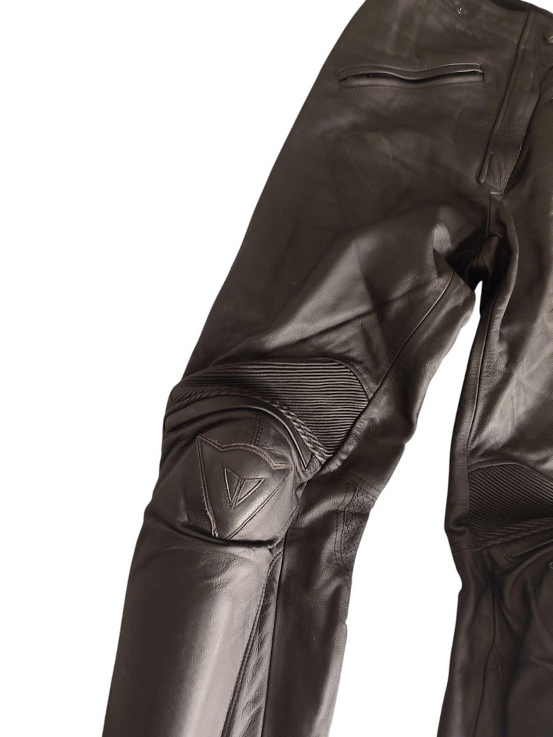 Może przedstawiać: Czarne sk&oacute;rzane spodnie motocyklowe ze wzmocnieniami kolan i szytym wzorem. Spodnie posiadają widoczne logo na kolanie i są przeznaczone do ochrony i trwałości. Wykonane z wytrzymałego materiału.