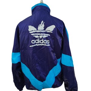 May include: A vintage Adidas track jacket in a striking colour scheme. The jacket has a deep purple base with turquoise blue accents on the sleeves and sides. The Adidas logo is displayed in white on the back.