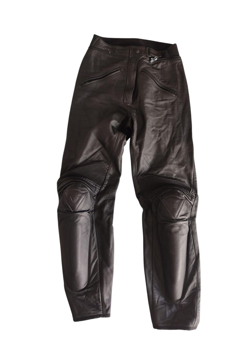 Może przedstawiać: Czarne sk&oacute;rzane spodnie motocyklowe z ochraniaczami kolan. Spodnie mają kieszenie zapinane na zamek i wzmocnione panele na kolanach. Ochraniacze kolan mają tr&oacute;jkątne logo.