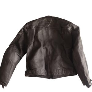 Może przedstawiać: Brązowa sk&oacute;rzana kurtka motocyklowa. Kurtka ma klasyczny kr&oacute;j z wysokim kołnierzem, wyściełanymi ramionami i paskiem w talii. Z tyłu widoczne jest logo. Kurtka wykonana jest z wytrzymałej sk&oacute;ry.