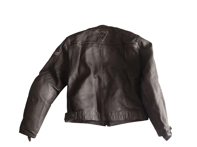 Może przedstawiać: Brązowa sk&oacute;rzana kurtka motocyklowa. Kurtka ma klasyczny kr&oacute;j z wysokim kołnierzem, wyściełanymi ramionami i paskiem w talii. Z tyłu widoczne jest logo. Kurtka wykonana jest z wytrzymałej sk&oacute;ry.