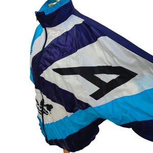 May include: A vintage track jacket in shades of blue, white, and purple, featuring a large black number 4. The jacket has a zip-up front and a stand-up collar. The jacket is displayed on a mannequin.