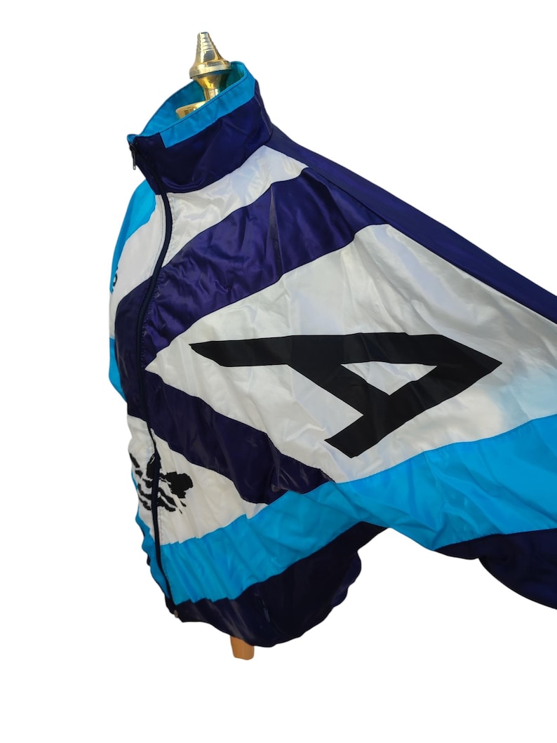 May include: A vintage track jacket in shades of blue, white, and purple, featuring a large black number 4. The jacket has a zip-up front and a stand-up collar. The jacket is displayed on a mannequin.