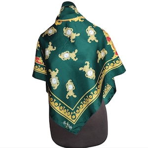 May include: A dark green silk scarf featuring a repeating pattern of gold clock designs. The scarf has a gold border with a repeating floral pattern and the text "After Eight" at the bottom.