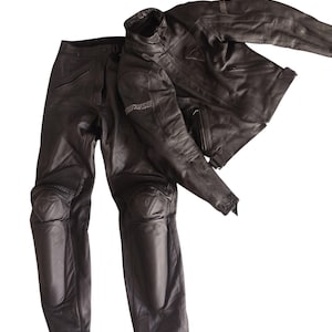 Może przedstawiać: Czarny sk&oacute;rzany zestaw kurtki i spodni motocyklowych. Kurtka ma st&oacute;jkę, a spodnie ochraniacze kolan. Zestaw wykonany jest z wytrzymałego materiału i został zaprojektowany z myślą o ochronie. Nazwa marki jest widoczna na kurtce.