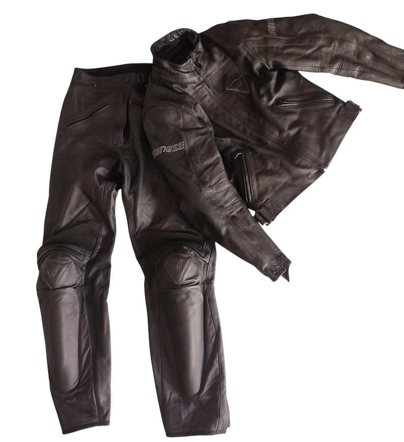 Może przedstawiać: Czarny sk&oacute;rzany zestaw kurtki i spodni motocyklowych. Kurtka ma st&oacute;jkę, a spodnie ochraniacze kolan. Zestaw wykonany jest z wytrzymałego materiału i został zaprojektowany z myślą o ochronie. Nazwa marki jest widoczna na kurtce.