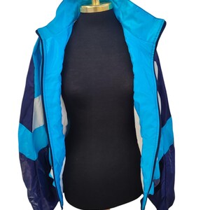 May include: A vintage track jacket in shades of blue, navy, and white, displayed on a mannequin. The jacket features a high collar, a full zip, and a colour-blocked design. The jacket is made of a lightweight material, perfect for layering.