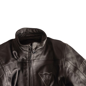 Może przedstawiać: Czarna sk&oacute;rzana kurtka motocyklowa ze st&oacute;jką i zapięciem na zamek błyskawiczny. Kurtka posiada tr&oacute;jkątne logo na piersi oraz nazwę marki na rękawie. Sk&oacute;ra ma teksturowany wygląd.