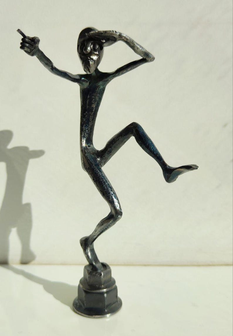 May include: A dark metal sculpture of a person in a dynamic pose, with one arm extended and the other hand shading the eyes. The figure is mounted on a hexagonal base, creating a striking contrast.