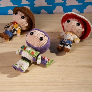 Puede incluir: Tres personajes de juguete de crochet de la franquicia Toy Story. Woody lleva un sombrero de vaquero rojo y blanco y un chaleco azul y amarillo. Buzz Lightyear lleva un casco morado y un traje espacial verde y blanco. Jessie lleva un sombrero de vaquero rojo y blanco y un chaleco amarillo y azul.
