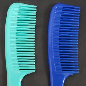 May include: Two plastic hair combs. One is a bright teal color, and the other is a deep blue. Both combs have a curved handle and closely spaced teeth, designed for detangling and styling hair. The combs are shown against a dark background.