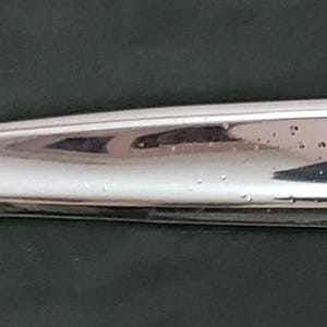 May include: A shiny, chrome-colored car part, possibly a trim piece or handle, with a curved shape and a recessed center section. The object reflects light, suggesting a polished finish.