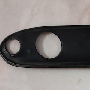 May include: A black, elongated rubber part with three holes. The part has a rectangular shape with rounded ends. The text "1-3001-1200" is visible on the surface. The part appears to be a component of a larger item.