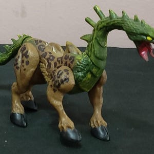 Könnte beinhalten: Zwei Spielzeug-Monsterfiguren. Eine ist rot mit großen Flügeln und einer gelben Flamme. Die andere ist beige mit braunen Flecken, grünen Akzenten und einem grünen Kopf mit offenem Maul.