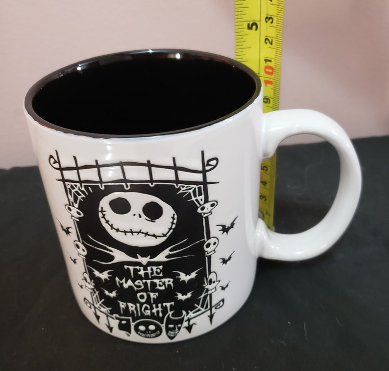 May include: White ceramic mug with a black interior and a curved handle. The mug features a black and white graphic of Jack Skellington from The Nightmare Before Christmas, with the text "THE MASTER OF FRIGHT".