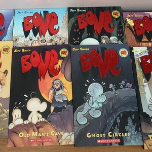 Op de afbeelding: Een verzameling van acht Bone graphic novels van Jeff Smith, uitgegeven door Scholastic. De covers bevatten diverse illustraties van witte, afgeronde personages in verschillende omgevingen, met het rode Bone-logo op elk boek.